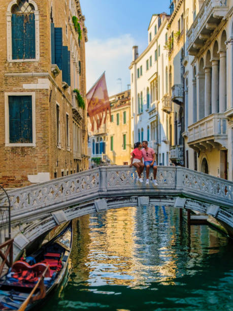 paar männer und frauen auf einer städtereise in venedig, italien, sitzend an einer brücke über den kanälen von venedig - men gondolier people activity stock-fotos und bilder