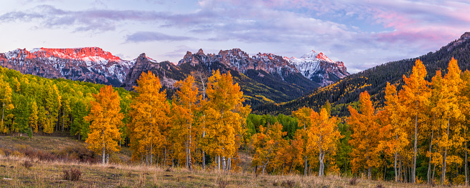 Alpenglow hits the ridglines above the Silver Jack Reservoir at sunset behind a line of colorful Autumn aspen trees in the Uncompahgre National Forest near Ridgway, Colorado.