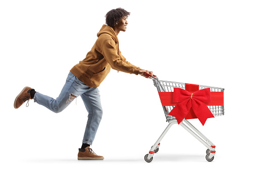 Full length profile shot of a young african american man running with a christmas shopping cart isolated on white background
