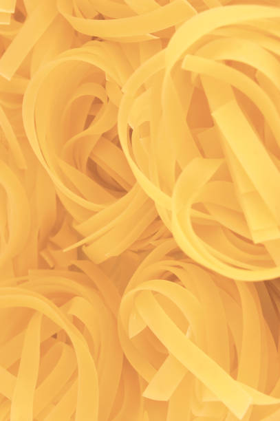 Traditional fettuccine ribbons pattern background, large detailed vertical raw dry long uncooked egg pasta macro closeup, natural golden texture diminishing perspective