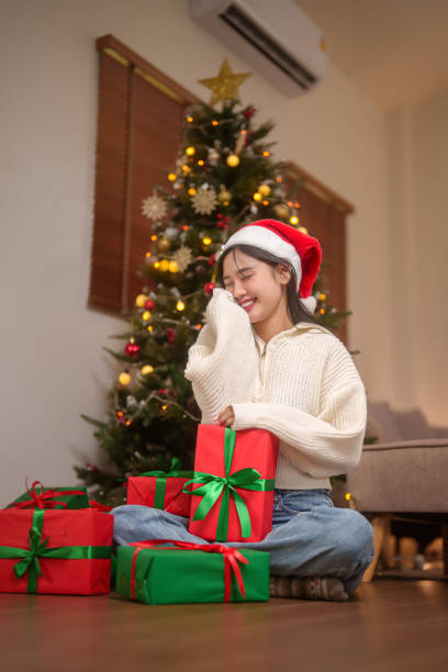 Asian women wearing sweater and santa hat smiling and holding presents with happiness while sitting in living room decorated with toys ornament for celebrate xmas tradition and holiday season at home. mujeres asiáticas con suéter y gorro de papá noel sonriendo y sosteniendo regalos con felicidad mientras están sentadas en la sala de estar decoradas con adornos de juguetes para celebrar la tradición navideña y la temporada navideña en casa