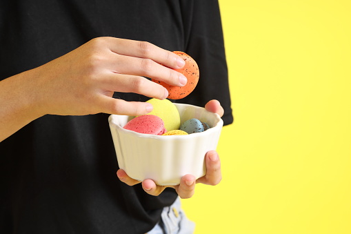 The Asian woman eating macaroons from the hand on the yellow background.