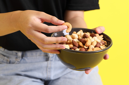 The Asian woman holding nuts on the yellow background.