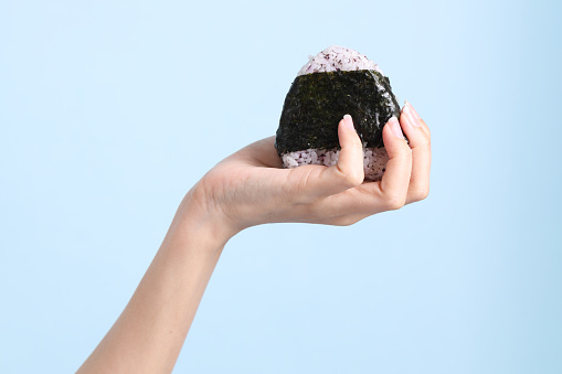 The Asian woman holding onigiri on blue background.