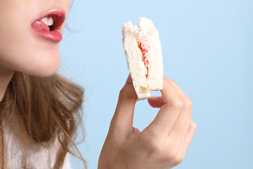The Asian woman eating sandwiches on blue background.
