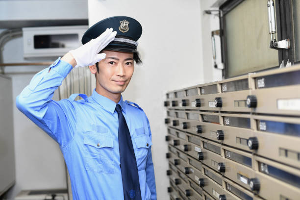 A young Asian man, a patrolling security guard wearing a hat and uniform, salutes in front of the post