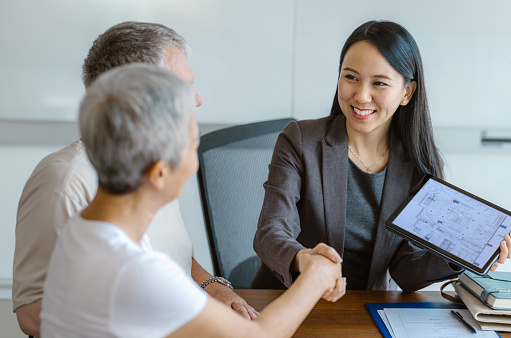 Multiethnic senior couple handshake with an Asian female real estate agent at sale office. - Real estate x Client consultation in Southeast Asia Concept.
