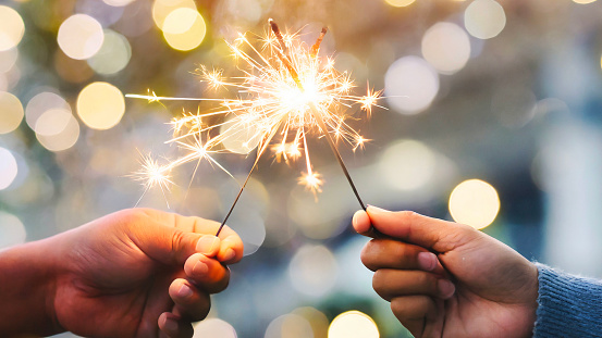 Adult hands holding burning sparklers against soft bokeh lighting and background in celebration of new year