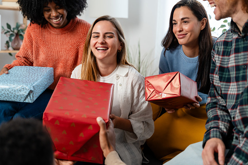 Group of young multiethnic friends with gift boxes sitting on sofa at home