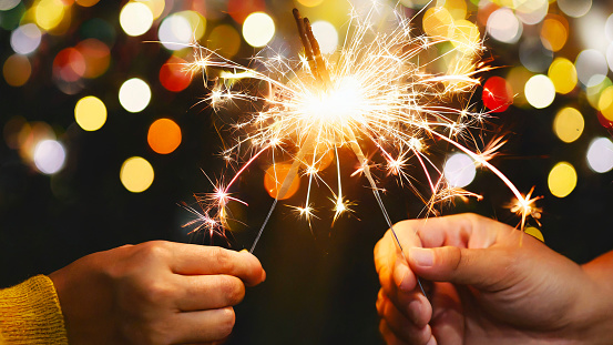 Adult hands holding burning sparklers against soft bokeh lighting and background in celebration of new year