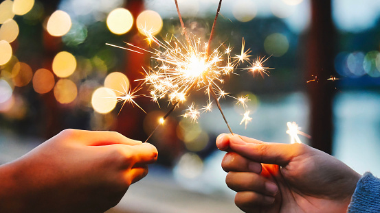 Adult hands holding burning sparklers against soft bokeh lighting and background in celebration of new year