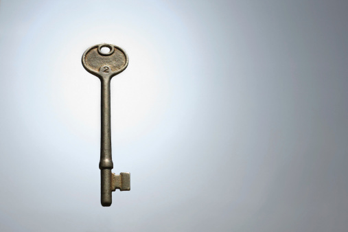 an antique silver skeleton key with the number two on it is illuminated and floating isolated against a white and gray background, with copy space for text