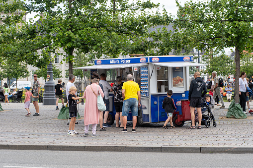 Copenhagen, Denmark - July 11, 2022: Customers at a traditional hot dog cart in the city centre.