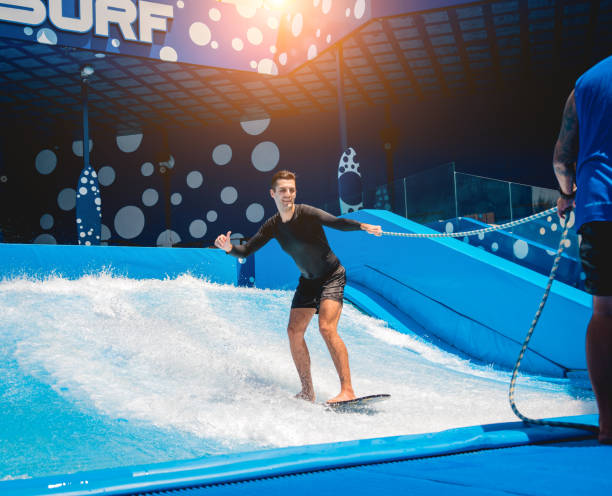 istock Young man surfing with trainer on a wave simulator at a water amusement park 1814383895