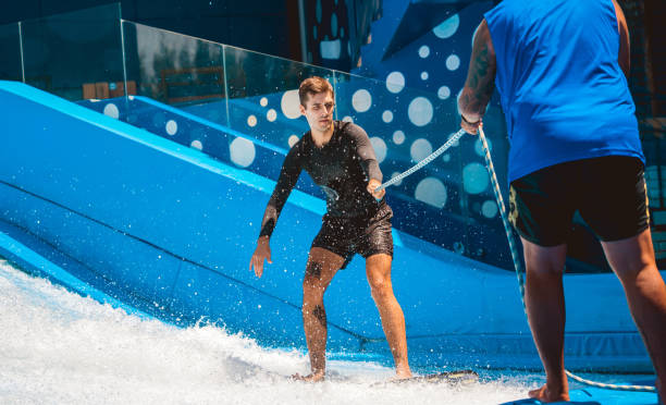 istock Young man surfing with trainer on a wave simulator at a water amusement park 1814385918