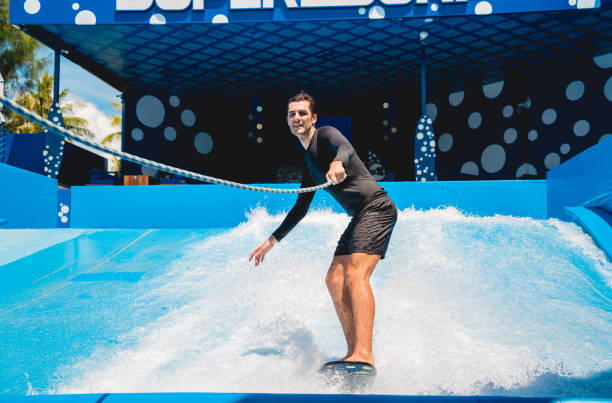 istock Young man surfing with trainer on a wave simulator at a water amusement park 1814386430