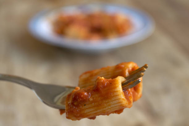 fork with rigatoni pasta with tomato sauce fork with rigatoni with tomato sauce and in the background a plate of pasta with sauce tomato rigatoni stock pictures, royalty-free photos & images