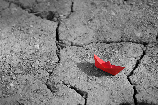 Red paper ship on cracked overdried soil
