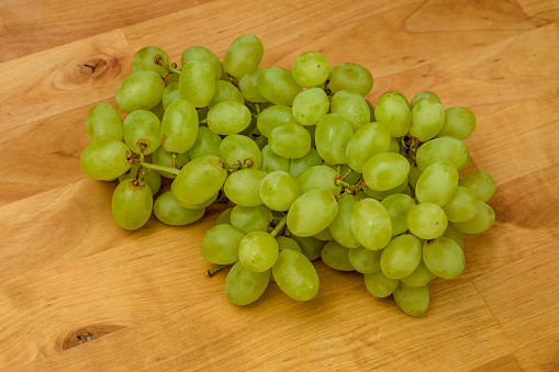 A bunch of ripe fresh green grapes lies on a wooden table closeup
