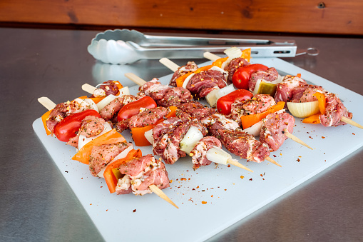Rohe Souvlaki Spieße mit Paprika und Zwiebel auf einem weißen Brett - raw pork skewers with pepper and onion on a white cutting board