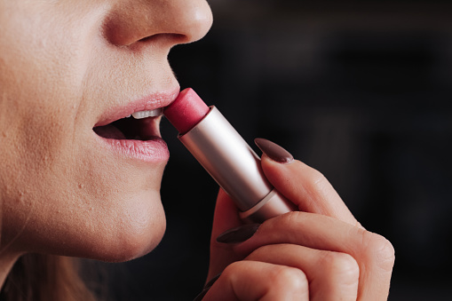 Applying pink lipstick. Face profile.