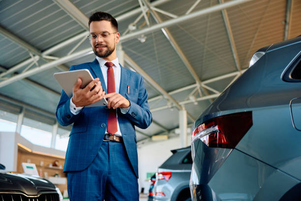 Car salesman working on digital tablet in a showroom.
