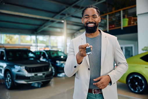 Happy African American man with keys of his new car in showroom looking at camera. Copy space.