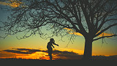 Silhouette pregnant woman standing with arms outstretched and head back by single bare tree against sky during sunset