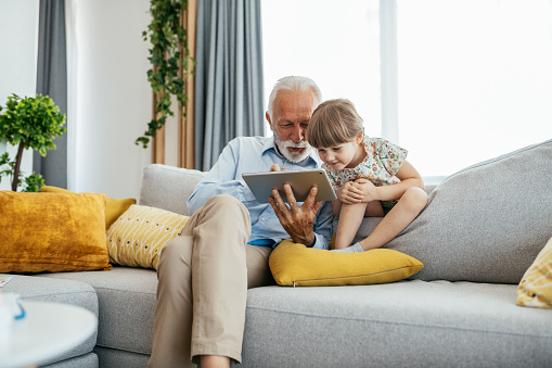 Image of senior man - grandfather and his granddaughter having fun at home