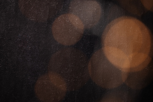 Abstract bokeh texture background with orange and brown circles from a garland on a dark antique backdrop close up. Circles of different sizes, blurred and out of focus. Free space for text.