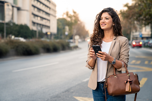 Outdoor shot of young woman using mobile phone outdoors in the city. Female business professional using smart phone in the city.
