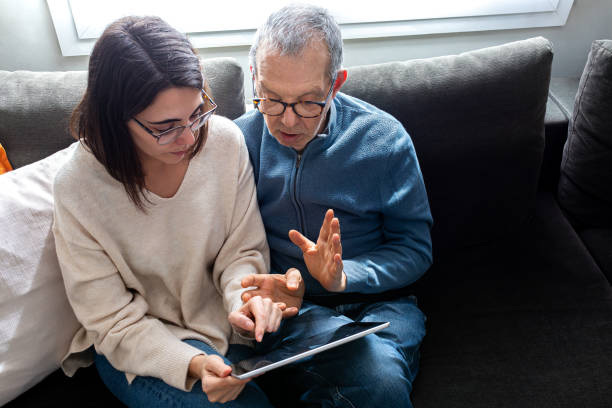 istock High angle view of senior father and young daughter using digital tablet together sitting on sofa in living room. 1814587573