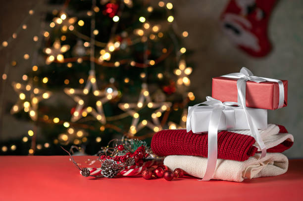 istock Christmas red and white gift boxes, knitted sweaters, pine tree decoration, candy canes on red table, blurred shiny Christmas tree on background. Holiday presents, Christmas eve celebration concept 1814605865
