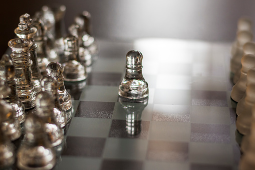 clear glass, transparent chess pieces on a checkerboard, selective focus, closeup, isolated on light