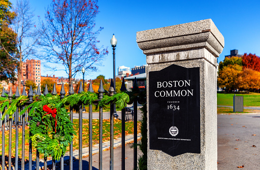 Boston, Massachusetts, USA - November 20, 2023: Close-up of the sign on a Boston Common entrance gate pillar.  Boston Common Founded 1634. Green holiday wreath on iron fence.