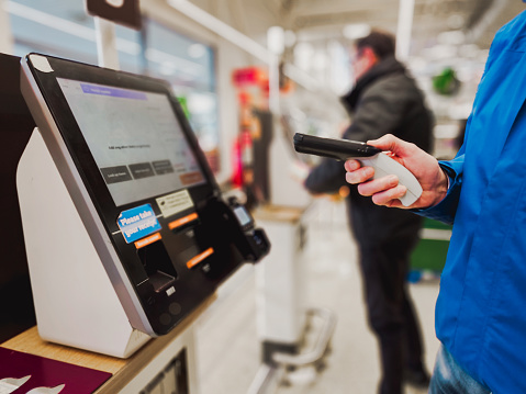 A senior man holding a bar code scanner in the supermarket at the self-checkout.