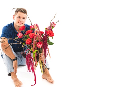 Man in casual clothes poses with a bouquet of flowers on a white studio background.