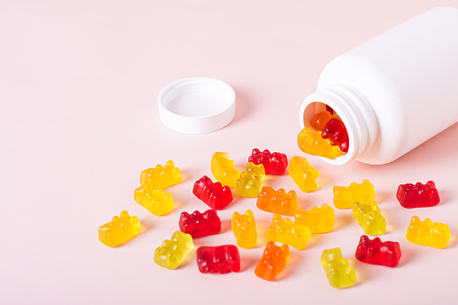 Group of gummy supplements with multivitamins and a bottle for them on a pink background