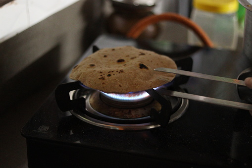 A Roti or chapati being cooked on the blue LPG flame with a roti picker