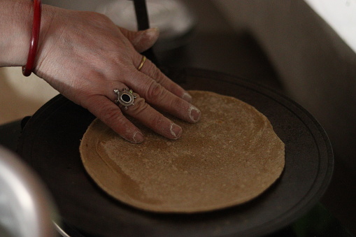 A Roti or chapati being cooked on the Black tawa or pan by a lady wearing ring