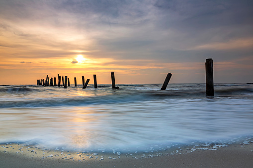 Silhouette view of the concrete columns of the old port with Beautiful sky sunrise and strong water waves on Sao Iang Beach at Phetchaburi province. Long exposure picture