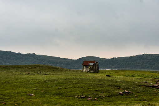 A small house in the middle of the grassland with hills behind.