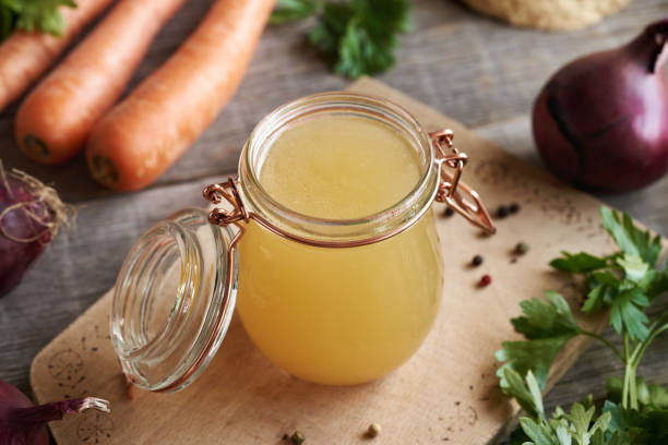 istock Bone broth in a transparent glass jar on a table, with fresh vegetables 1814786761