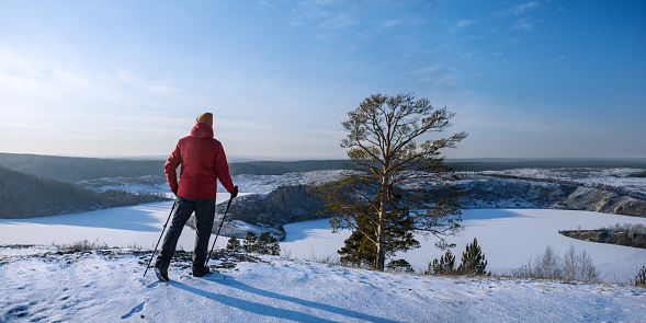 Male hiker hiking with nordic walking poles in snow-covered winter nature. Panoramic banner with copy space.