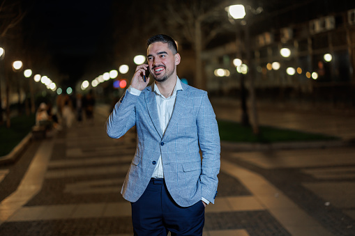 Immerse yourself in the urban dialogues as a mid adult man engages in a phone call amidst the captivating nighttime ambiance