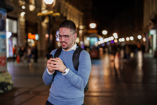 Discover the realm of digital dialogues as a mid adult man immerses himself in SMS conversations, typing away on his phone amidst the vibrancy of the night streets
