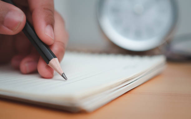 istock Human hands writing notes with pencil on paper on wooden table surface. 1814814662