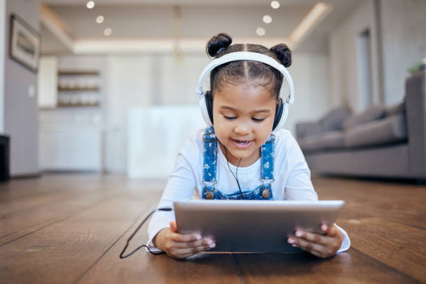 istock Kid, headphone and tablet for streaming in home with internet for entertainment, learning or watching. Little girl, lying and floor in living room for comfort with technology for online, web or app 1814817500