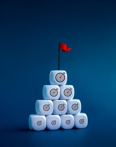 Accomplishing small business goals go to the big goal for victory, leadership and organization development concepts. Many sizes of target icons on wooden cube blocks pyramid shape with flag on top.