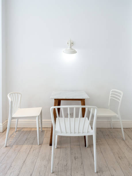 istock Vintage light lamps hanging on white wall over the empty dining table set with marble top table with wood legs and three chairs, minimal style living room. Bright cafe or restaurant interior decor. 1814818017